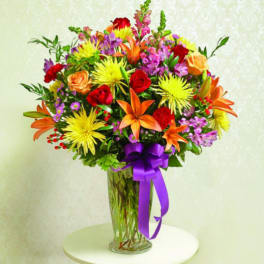 Colorful mixed bouquet in a clear glass vase with a purple ribbon