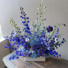 Blue and purple floral arrangement in a white rectangular vase