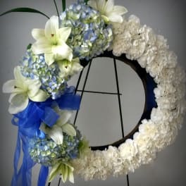 White floral wreath with blue hydrangeas, lilies, and a blue ribbon