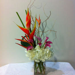 Tropical bouquet with red heliconia, purple calla lilies, and white hydrangea in a glass vase