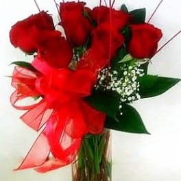 Red roses arranged in a clear glass vase with a red ribbon bow