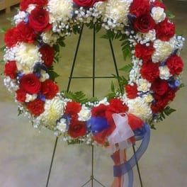 Heart-shaped floral wreath on a stand with red, white, and blue flowers