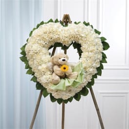 Heart-shaped white floral wreath with a teddy bear and ribbon on an easel