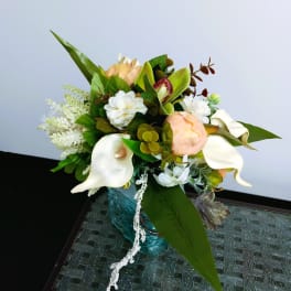 Bouquet with white calla lilies, peach roses, and green foliage in a blue vase.
