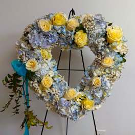 Heart-shaped floral wreath with yellow roses and blue hydrangeas on a stand