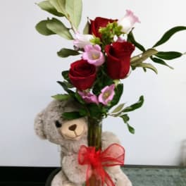 Red roses and pink flowers in a glass vase with a teddy bear
