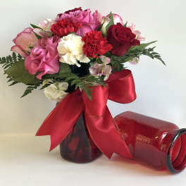 Pink and red bouquet in a red glass vase with a large ribbon