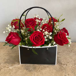 Red roses in a black handled gift bag with white baby's breath