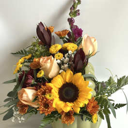 Mixed bouquet in a pale green pumpkin vase with a sunflower and peach roses