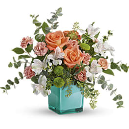 Peach and white flower arrangement with roses in a turquoise glass cube vase