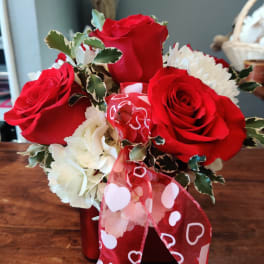 Bouquet of red roses and white flowers with a heart-patterned ribbon in a red vase