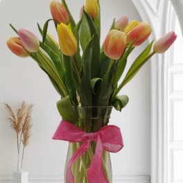 Bouquet of multicolored tulips in a clear glass vase with a pink ribbon
