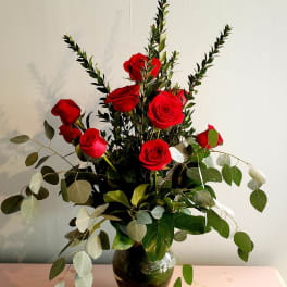 Red roses arranged in a dark glass vase with airy eucalyptus
