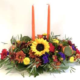 Low floral centerpiece with two tall orange candles and a sunflower