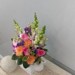 Pink and orange mixed flower arrangement in a white ceramic container