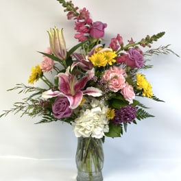 Mixed bouquet of lilies, roses, hydrangea, and daisies in a glass vase