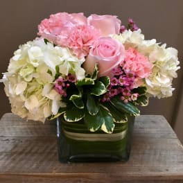 Pink roses and carnations arranged with white hydrangeas in a green glass vase.