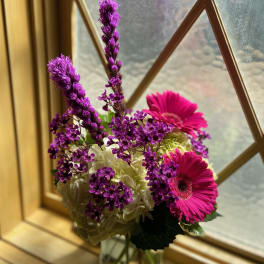 Pink gerbera daisies and purple flowers in a glass vase
