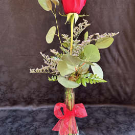 Single red rose in a clear vase with a pink ribbon
