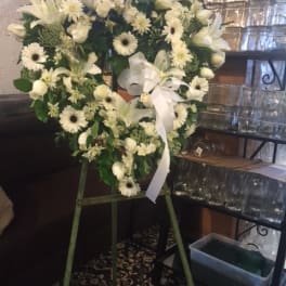 White floral wreath on a stand with a white ribbon bow