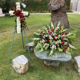 Two floral funeral tributes with red roses and white flowers outdoors