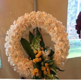 Large circular floral wreath of cream roses with yellow blooms at the base