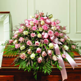 Pink and white rose casket spray with ribbon on a wooden casket
