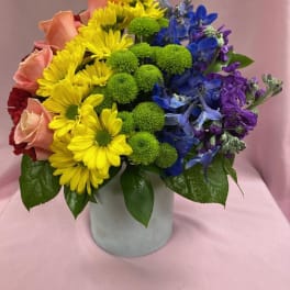 Colorful mixed bouquet in a white vase with yellow, blue, purple, and pink flowers