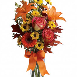 Orange lilies and pink roses in a glass vase with a ribbon