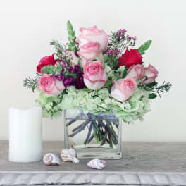 Pink and red roses in a clear glass vase with pale green hydrangeas