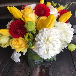 Bouquet of yellow tulips, red dahlias, white chrysanthemums, and yellow roses in a glass vase