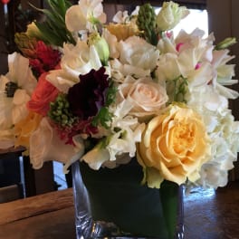 Mixed bouquet of white, yellow, pink, and burgundy flowers in a glass vase
