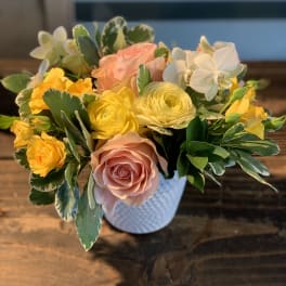 Mixed bouquet of pink, yellow, and white flowers in a white vase