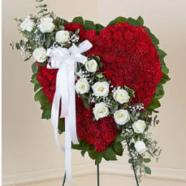 Heart-shaped red floral standing spray with white roses and a white ribbon bow on an easel.