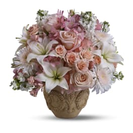 Round arrangement of pale pink roses, white lilies, and soft blooms in an ornate beige ceramic vase