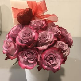 Pink roses in a white vase with a red ribbon and heart decoration
