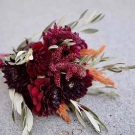 Deep red bouquet with orange accents and two rings on a stone surface