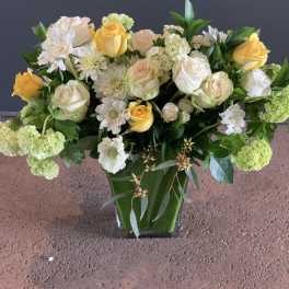 Yellow and white roses in a clear vase with mixed white blooms