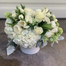 White floral arrangement in a round white vase with green accents