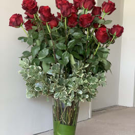 Tall vase arrangement of red roses with variegated greenery