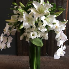 White lilies and orchids arranged in a tall glass vase