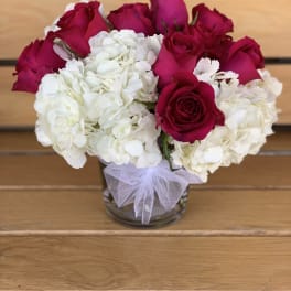 Red roses and white hydrangeas in a glass vase with a tulle bow