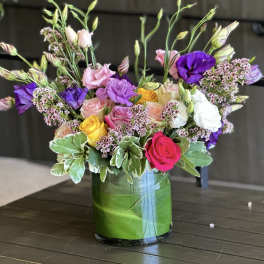 Mixed pink, purple, white, and yellow flowers in a glass vase