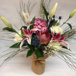 Mixed bouquet with lilies, hydrangea, and protea in a burlap-wrapped vase