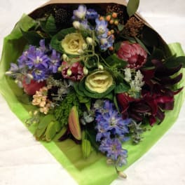 Mixed bouquet with purple, pink, and cream flowers wrapped in green paper
