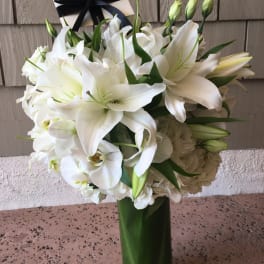 White lilies and orchids in a tall glass vase with a black ribbon