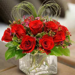 Red roses arranged in a clear square glass vase with decorative loops