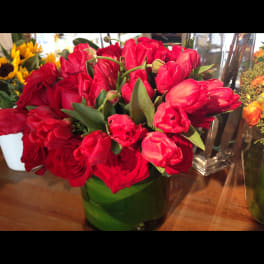 Red tulips and roses arranged in a green glass vase
