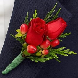 Red rose boutonniere with green accents on dark fabric
