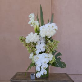 Tall white floral arrangement in a green vase with calla lilies and orchids